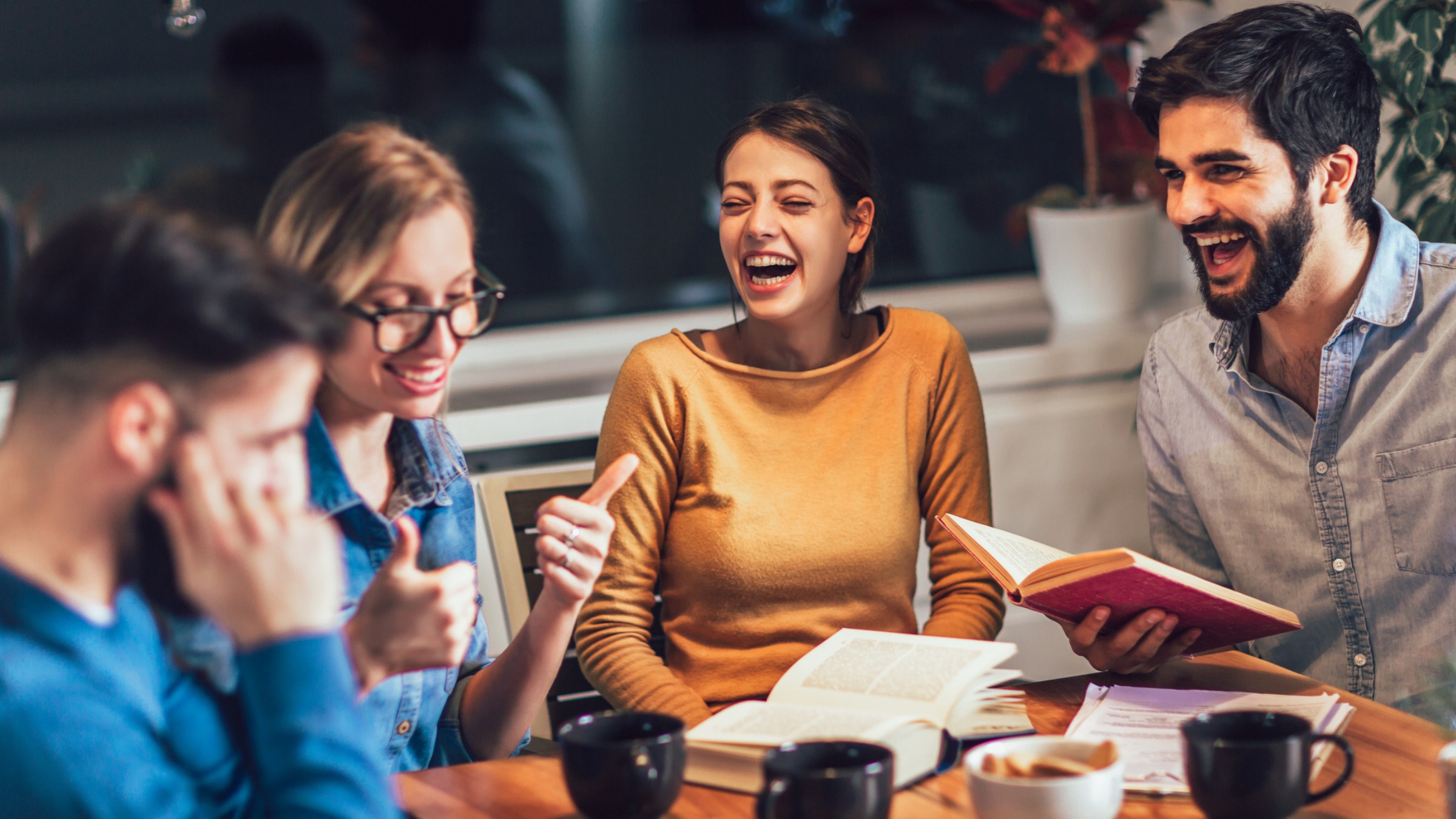 Friends laughing around a table with books and coffee during an evening discussion