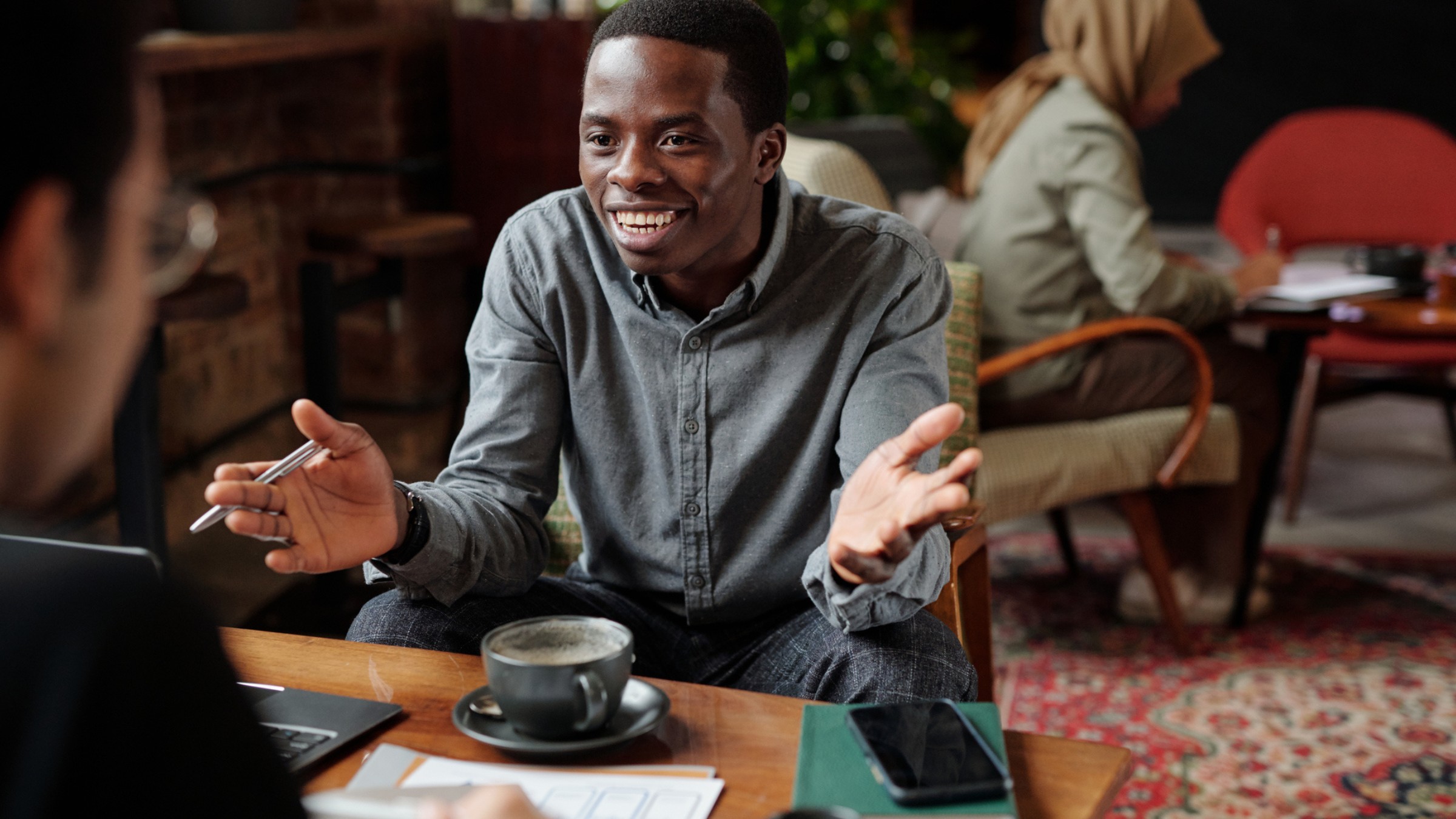 A man gesturing warmly while talking across a cafe table